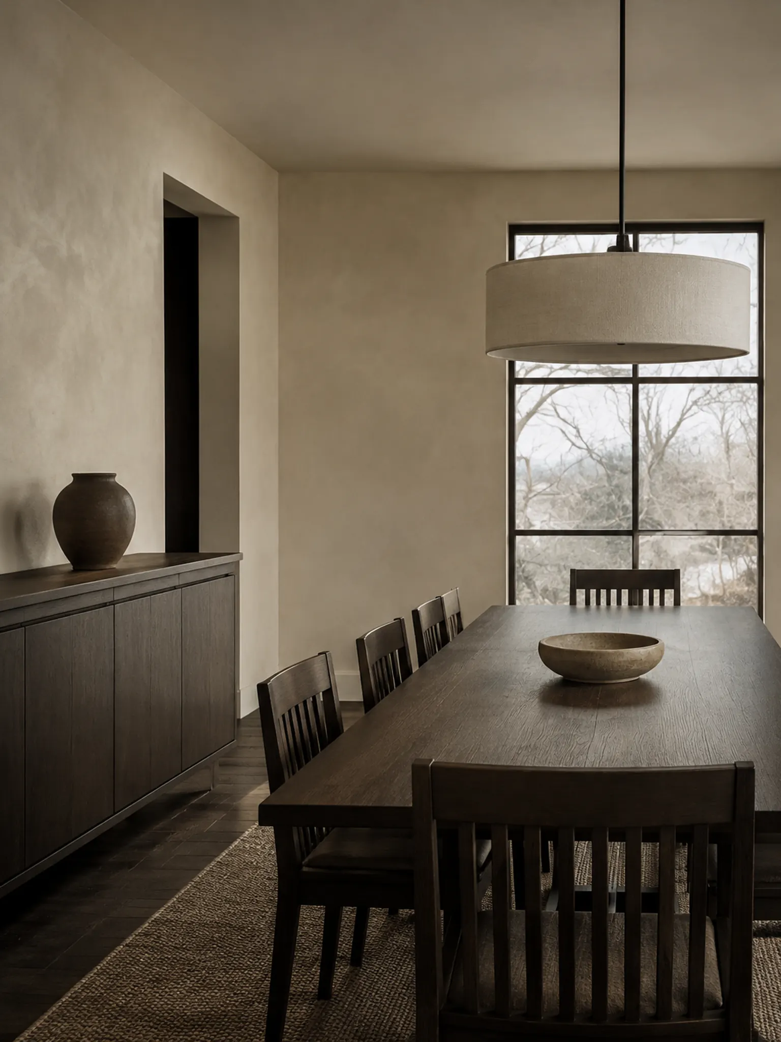 Dining room with an espresso-stained oak table, a long dark sideboard, slatted chairs and pale plaster walls