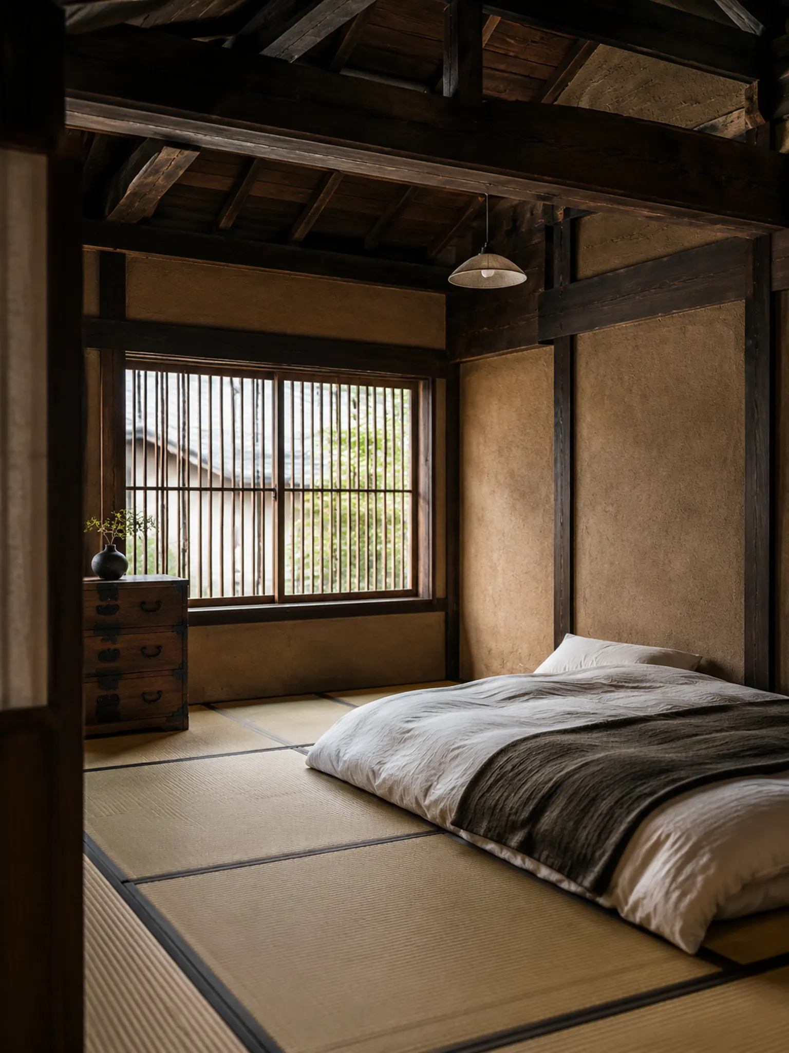 Bedroom in the style of a Kyoto machiya townhouse with dark timber posts and exposed beams, clay plaster walls, a latticed window, tatami floor, a futon and a wooden chest