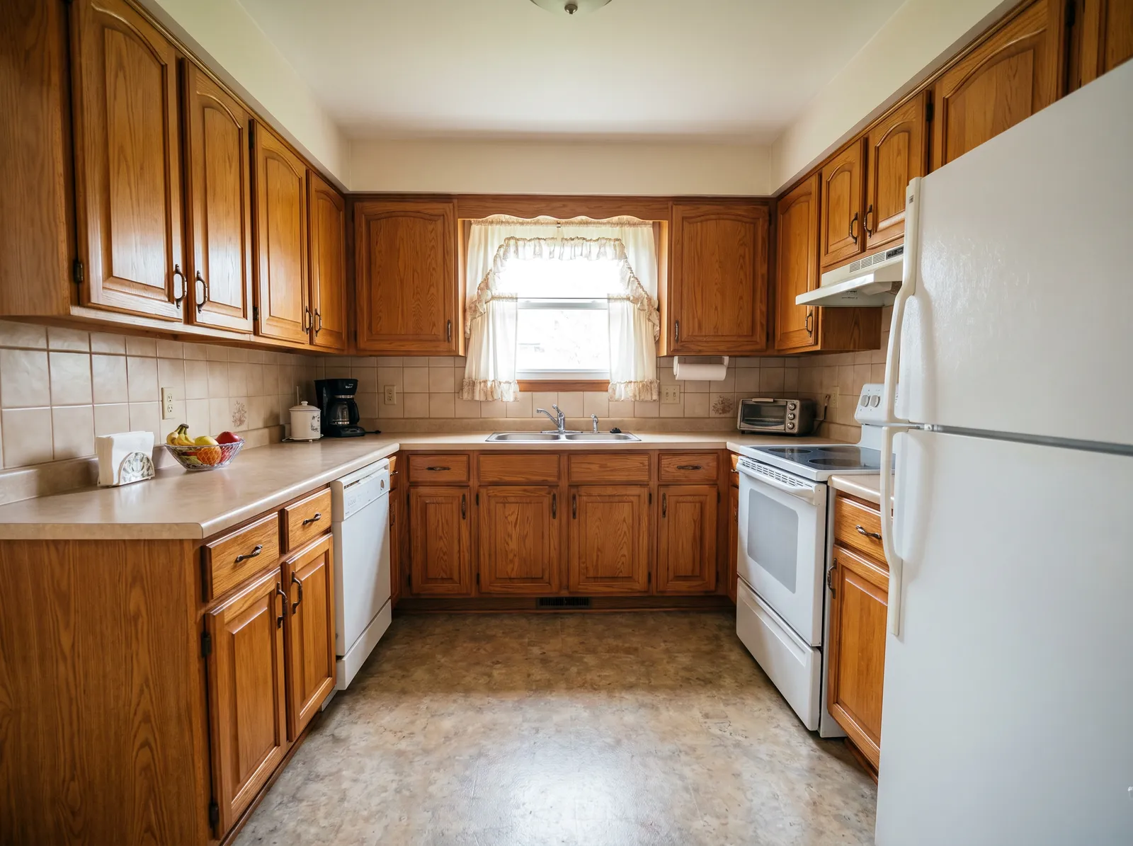 Before: a kitchen with orange-toned oak cabinets, beige counters and tile, and white appliances